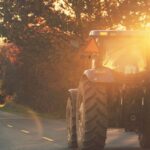 Tractor on a rural road at sunrise, surrounded by trees and warm light.