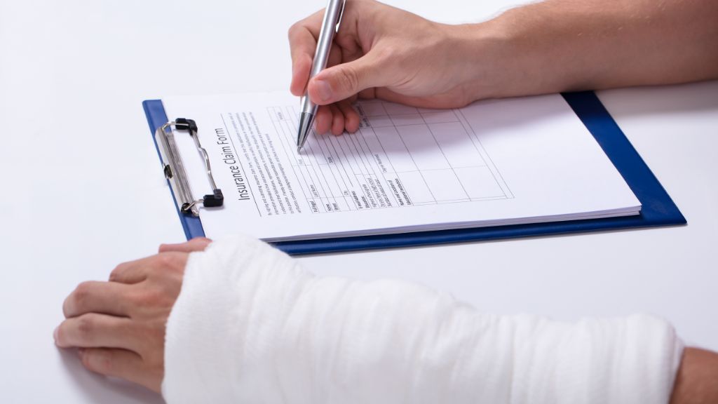 Person with bandaged arm filling out an insurance claim form on a clipboard.