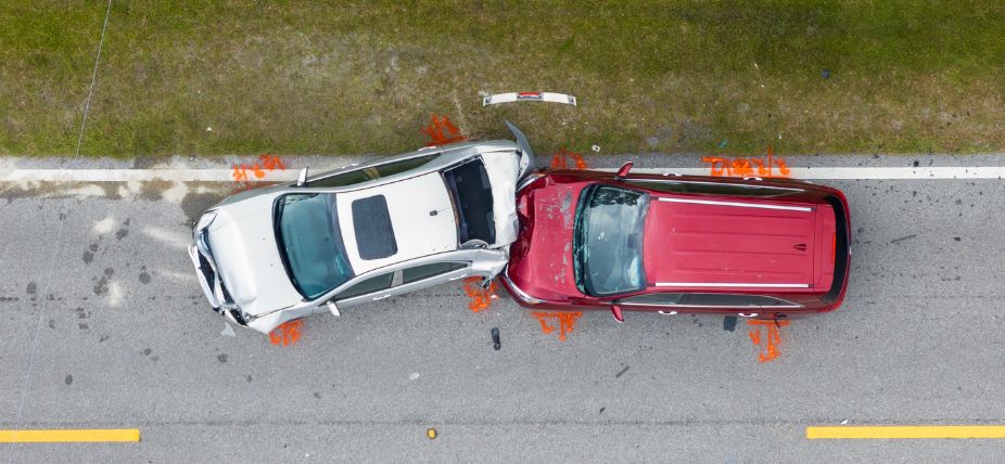 Overhead view of a car accident involving a red SUV and a silver car on a road with grassy roadside.