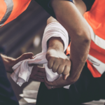 Workers in orange safety vests bandaging an injured arm on a construction site.