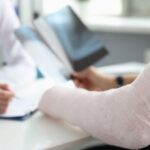 Patient with arm cast consults doctor holding X-rays at desk.