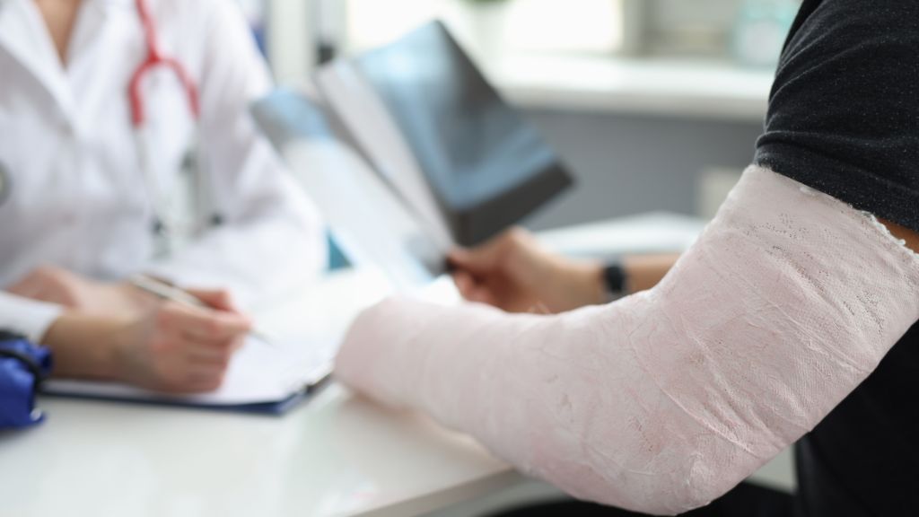 Patient with arm cast consults doctor holding X-rays at desk.