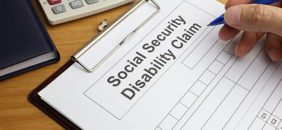 A person filling out a Social Security Disability Claim form on a clipboard, with a pen and calculator nearby.