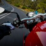 Motorcyclist in protective gear riding a red bike on a curvy road, surrounded by trees.
