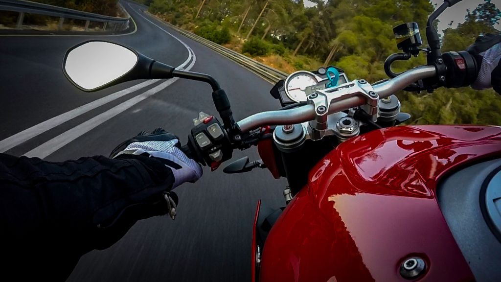 Motorcyclist in protective gear riding a red bike on a curvy road, surrounded by trees.