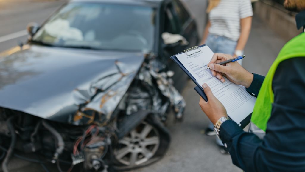Insurance agent assessing damage on a crashed car with a clipboard, next to an unidentifiable woman in a striped shirt.
