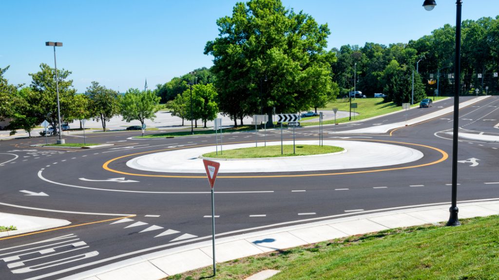Modern roundabout with clear road markings and lush greenery in a suburban area under a bright blue sky.