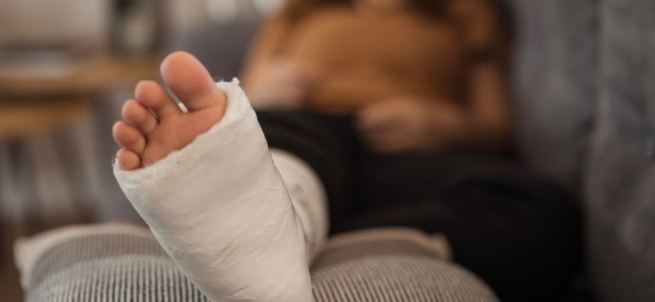 Close-up of a person's foot in a cast, resting on a cushion, with a blurred background.