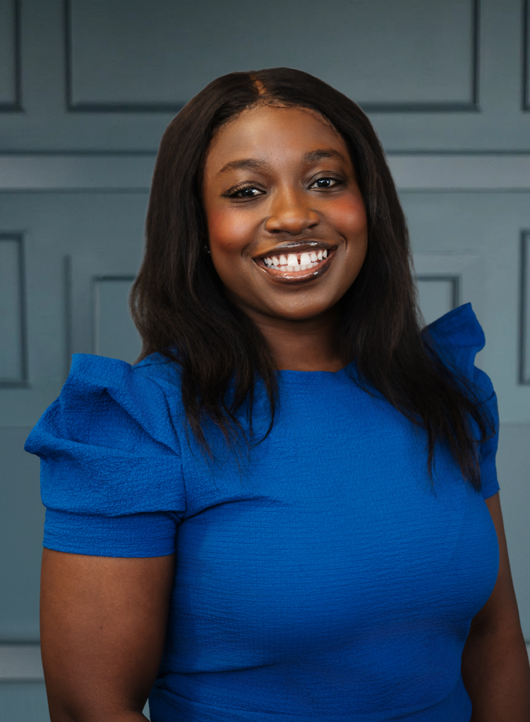 Smiling woman in blue dress against a paneled blue background.
