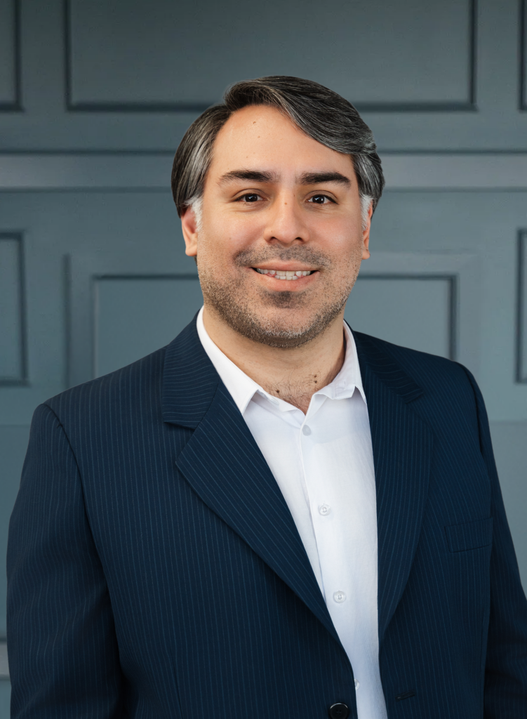 Smiling man in a suit with gray background, professional headshot portrait.