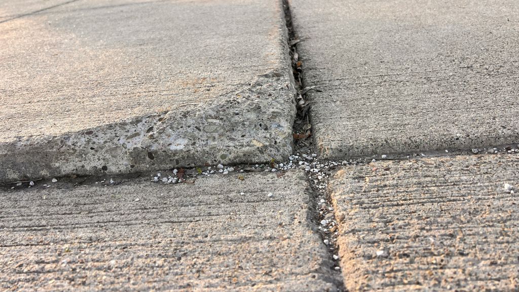 Uneven concrete sidewalk with noticeable cracks and granular debris.
