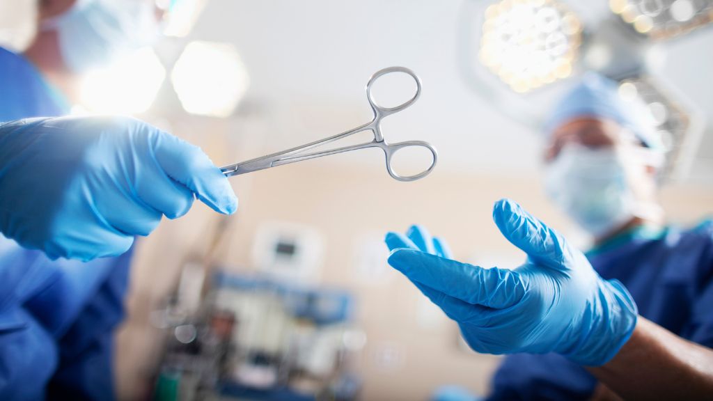 Surgeons in blue scrubs and gloves pass surgical scissors in an operating room.