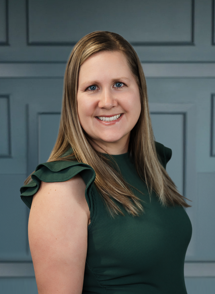 Smiling woman in a green ruffled top posing against a paneled gray background.