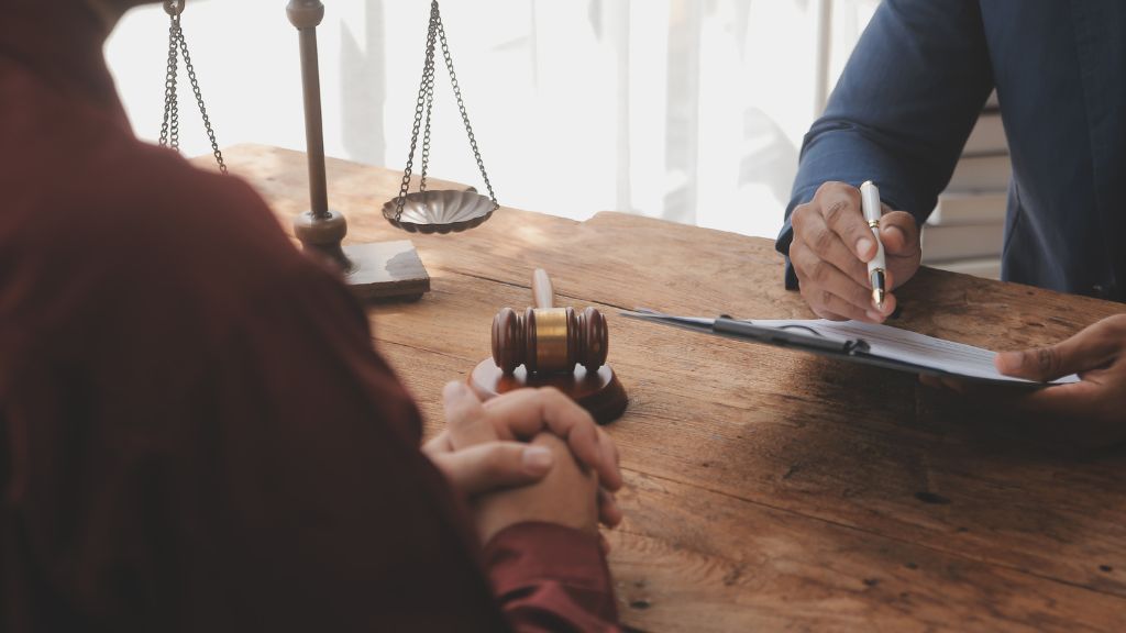 Two individuals discussing legal matters at a table with a gavel and scales of justice.
