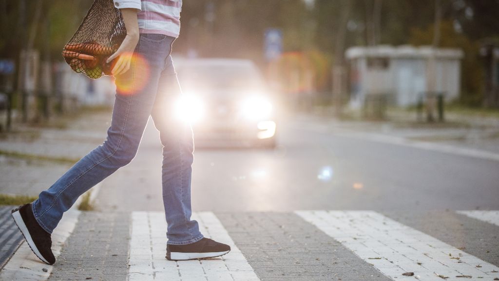 Person crossing street at crosswalk with car headlights shining. Carrying bag of groceries.